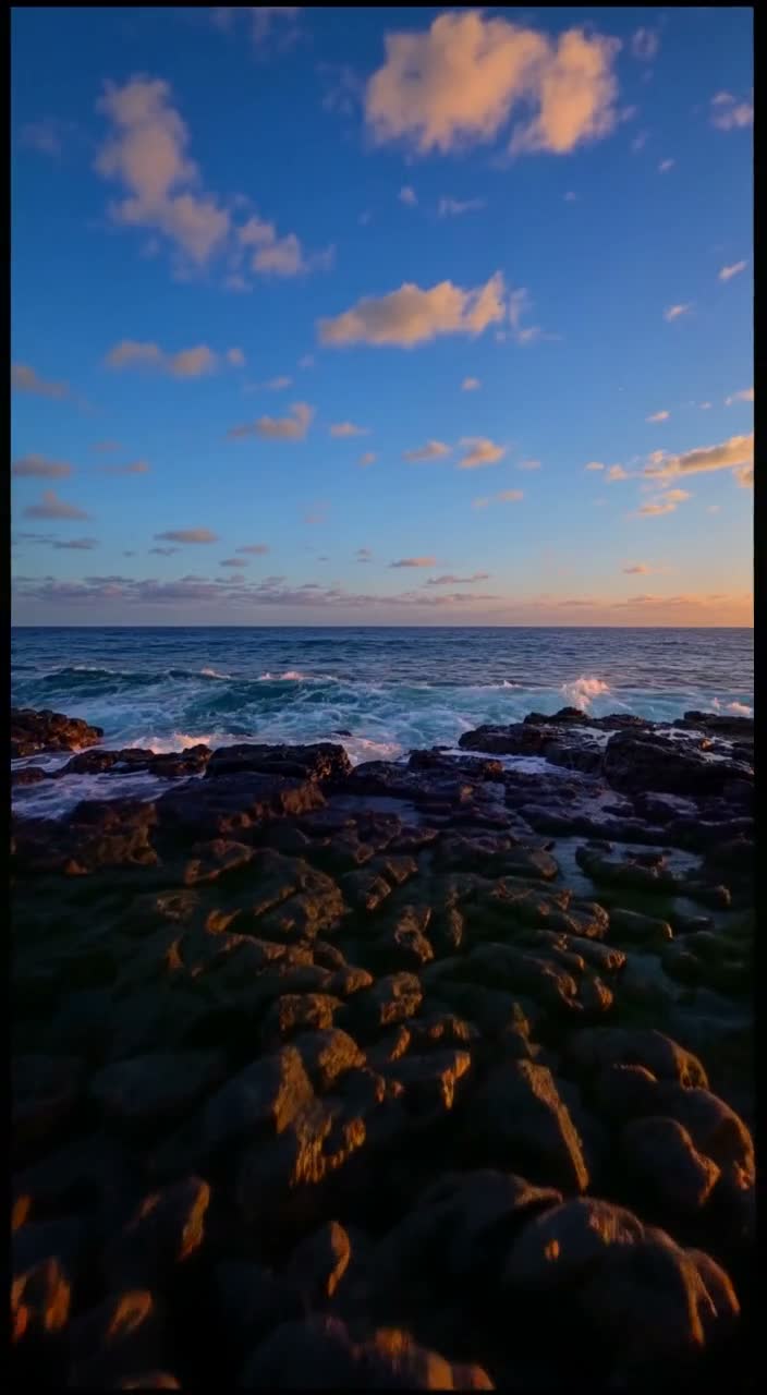 A portrait video of waves on volcanic rock, with an expanded dusk sky above and dark rock foreground below.